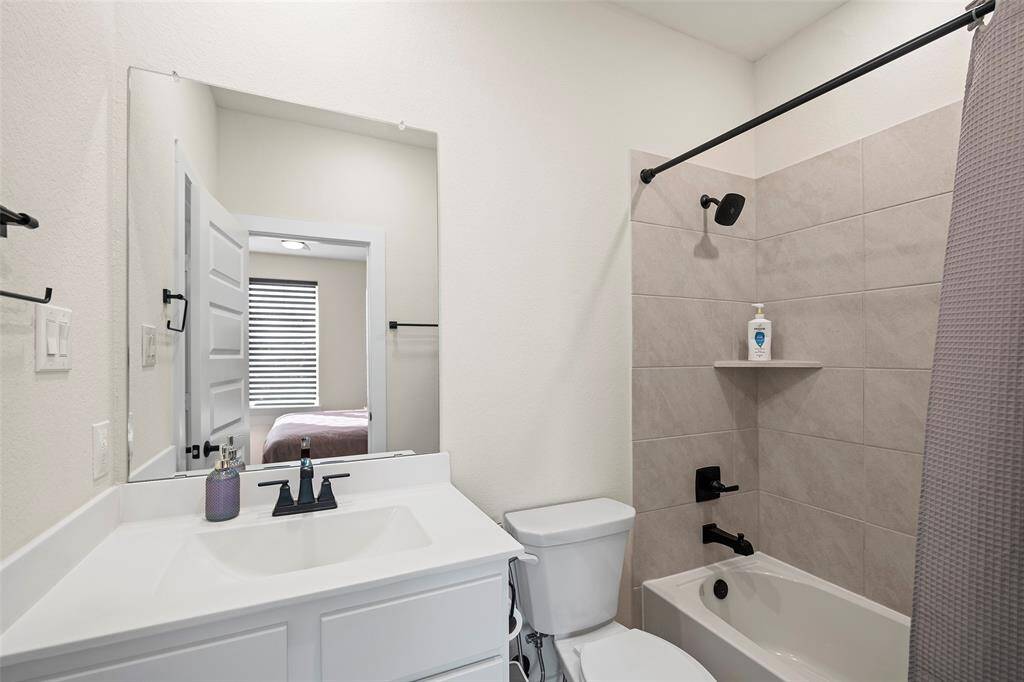 Full bathroom located upstairs, featuring a sleek vanity, modern matte black fixtures, and a tiled tub/shower combo with built-in shelving.