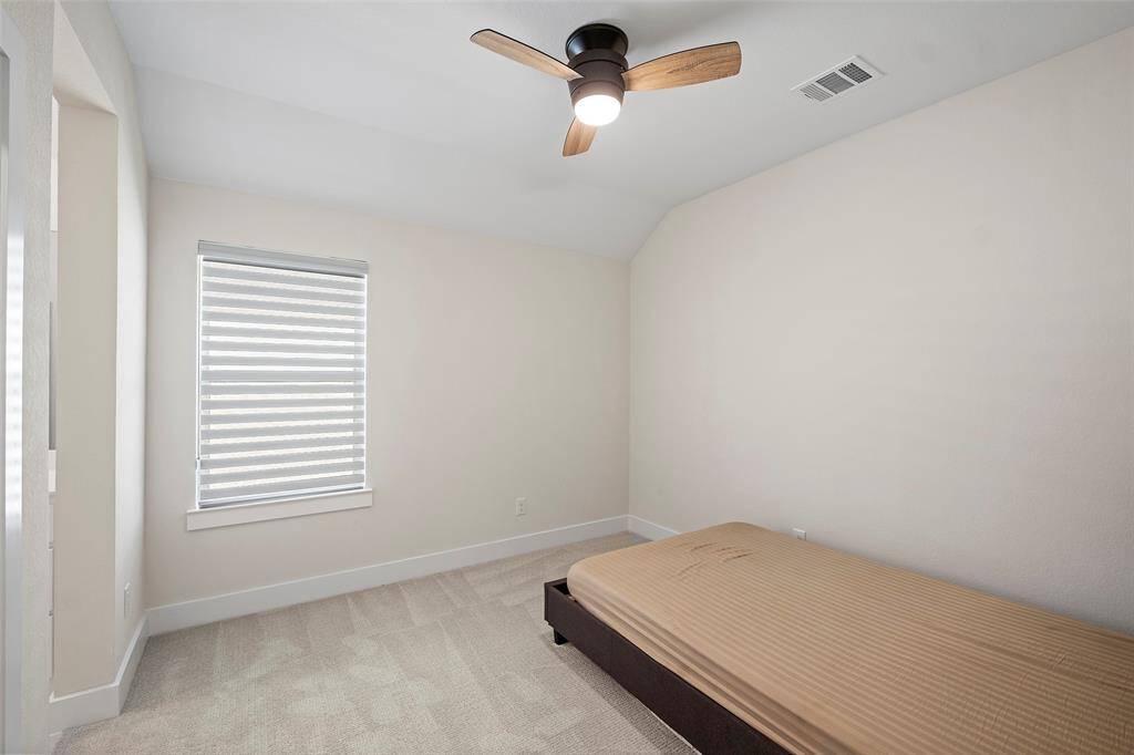 Another upstairs bedroom offers soft natural light, neutral tones, and a ceiling fan, making it a comfortable and versatile space for guests or family.