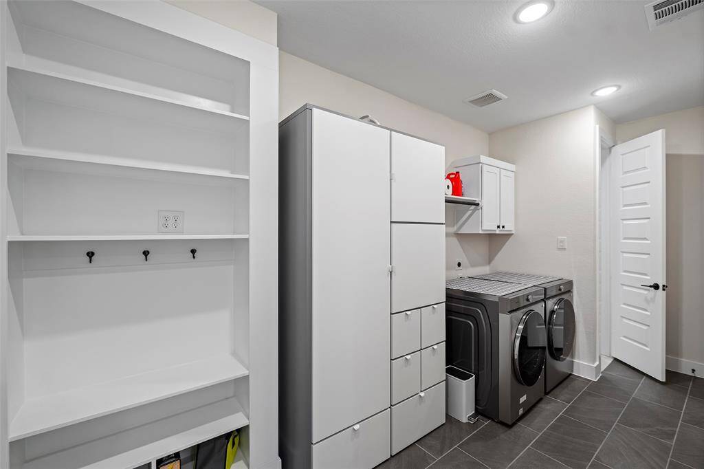 Spacious laundry room outfitted with full-size washer and dryer hookups, sleek tile flooring, and extensive built-in storage. Includes a mudroom drop zone with hooks and shelving, perfect for organizing everyday essentials.