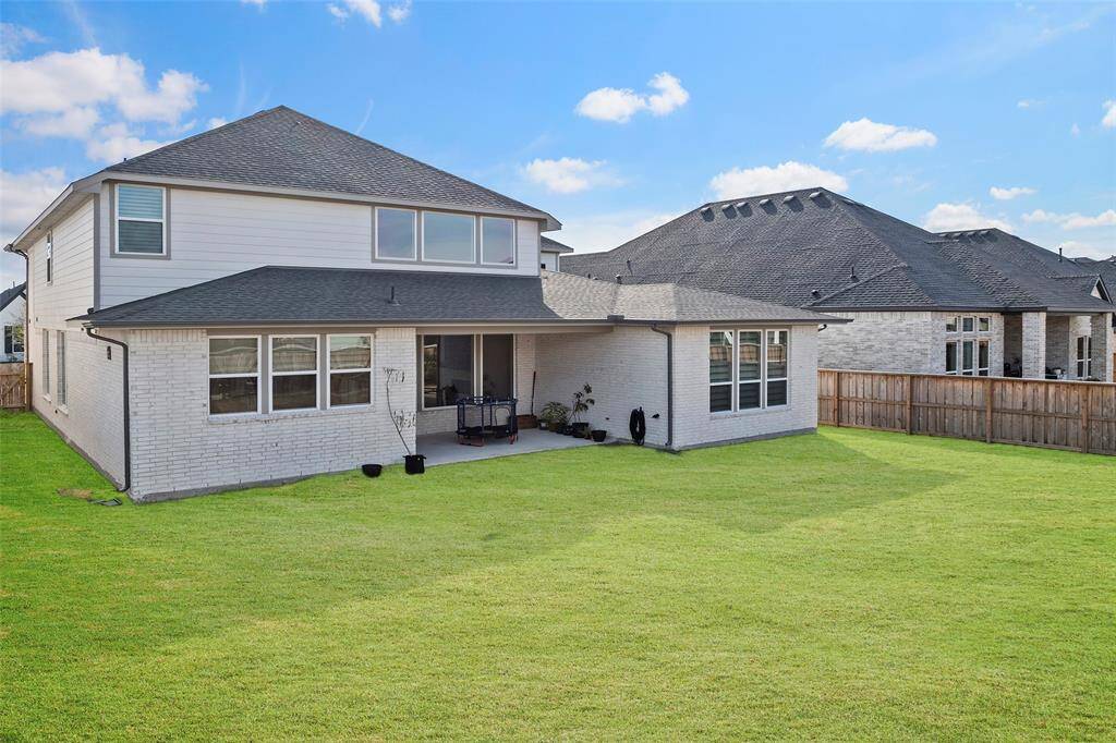 Covered patio extends from the rear elevation, offering a shaded spot to relax or entertain while overlooking the expansive backyard. Brick exterior and clean lines complement the modern design of the home.