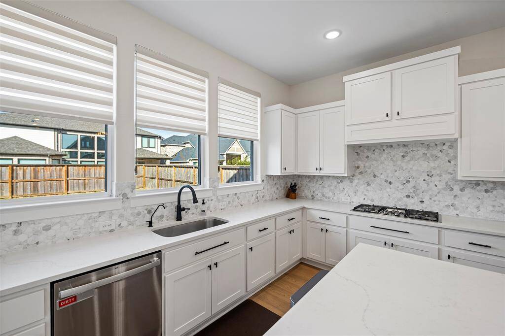 Closer look reveals thoughtful design details, from the mosaic tile backsplash to the under-cabinet lighting and matte black hardware. Generous counter space and abundant cabinetry make this kitchen as practical as it is polished.