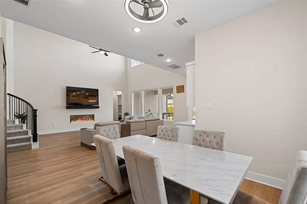 Towering ceilings and oversized windows fill the open-concept living and dining areas with natural light. A sleek electric fireplace adds a modern touch, while the curved staircase anchors the space with elegance and flow.