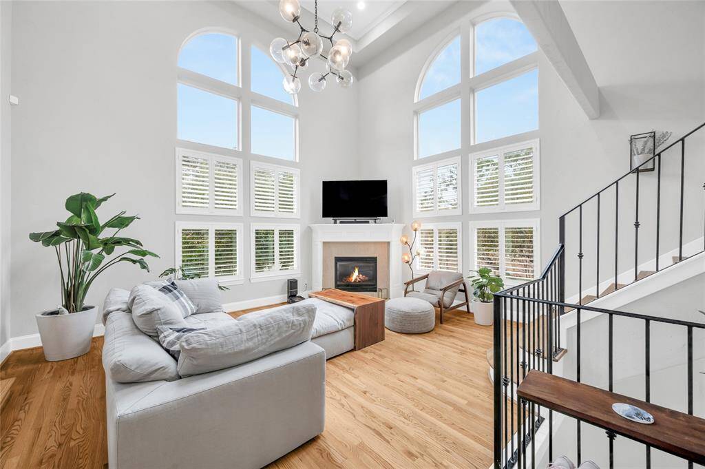 The sunlit living room offers plenty of space for large scale furniture, gas log fireplace, two-story windows, and handsome fixture that conveys with the home.