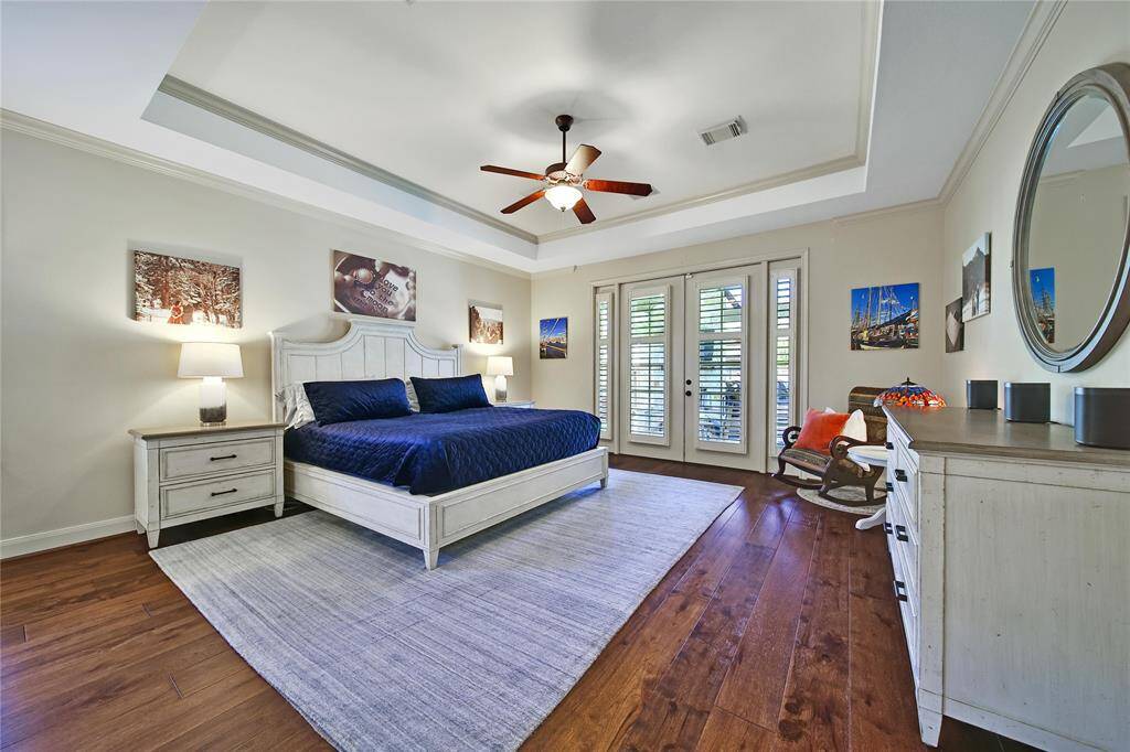 Spacious primary suite with tray ceiling and wide plank wood flooring plus direct access to the outdoor oasis.