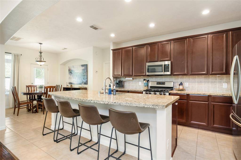 This thoughtfully designed kitchen blends timeless finishes with everyday functionality, featuring rich wood cabinetry, granite countertops, and sleek stainless steel appliances. A generous island offers additional prep space and casual seating, while the adjacent dining area is filled with natural light—creating a warm and inviting atmosphere at the heart of the home.