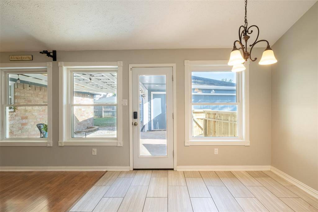 Bright breakfast area with large windows and a glass door leading to the patio. Features a mix of wood and tile flooring.