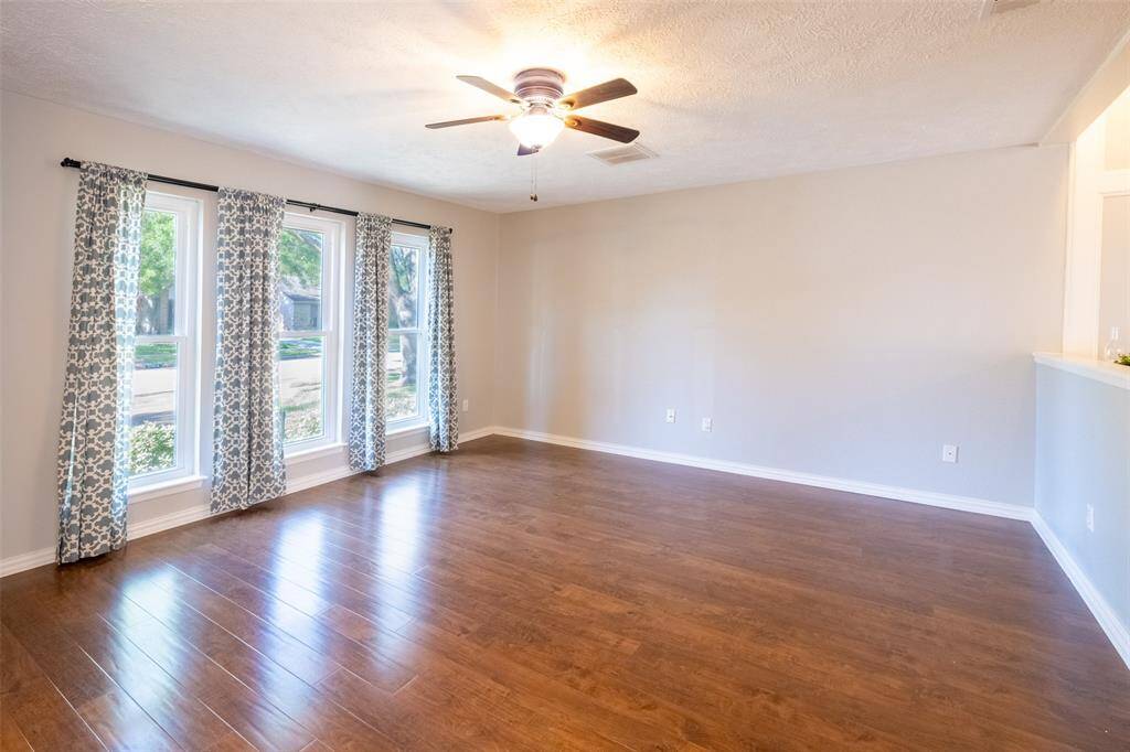 Bright and spacious living room with large windows, hardwood floors, neutral walls, and a ceiling fan, perfect for comfortable living.