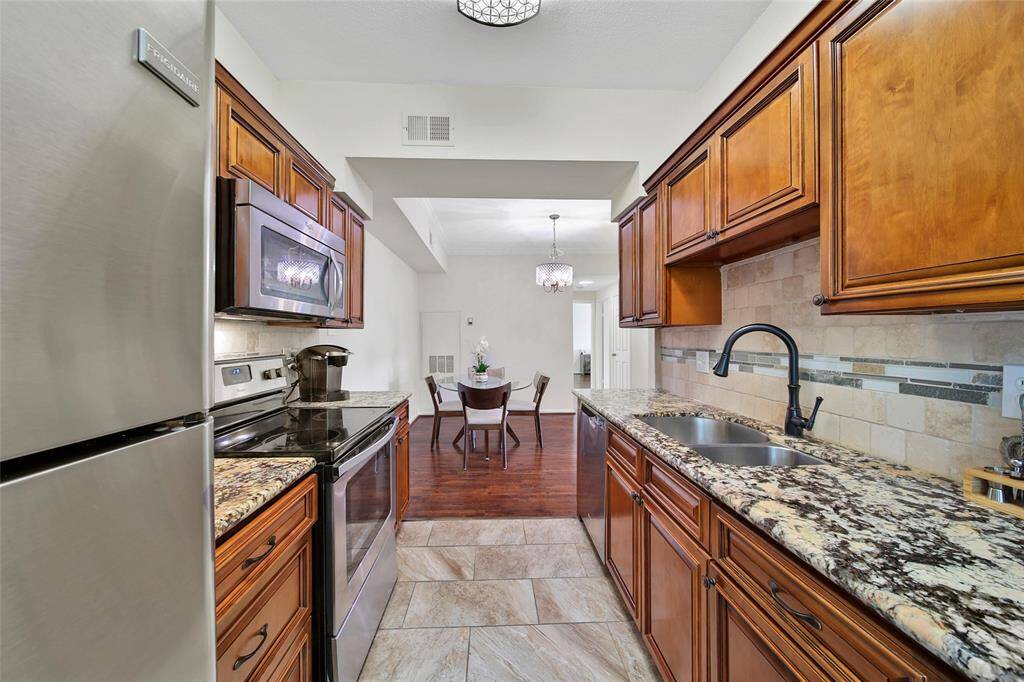 All appliances are included in the kitchen, including a stainless steel range with microwave, stainless steel dishwasher, and stainless steel fridge. Note the charming oil rubbed bronze hardware tying in the cabinetry with the arched faucet.