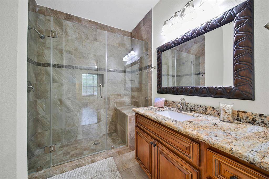 The primary bathroom was remodeled to offer a spacious frameless glass spa-style shower. An extended vanity with granite top matches the kitchen cabinetry and is accented by a beautiful framed mirror.