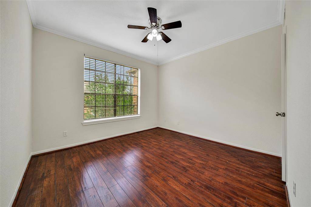 The second bedroom features gleaming wood look flooring, fresh neutral paint with crown molding, light filled tree-lined views, a ceiling fan for additional temperature control, and a closet for storage.