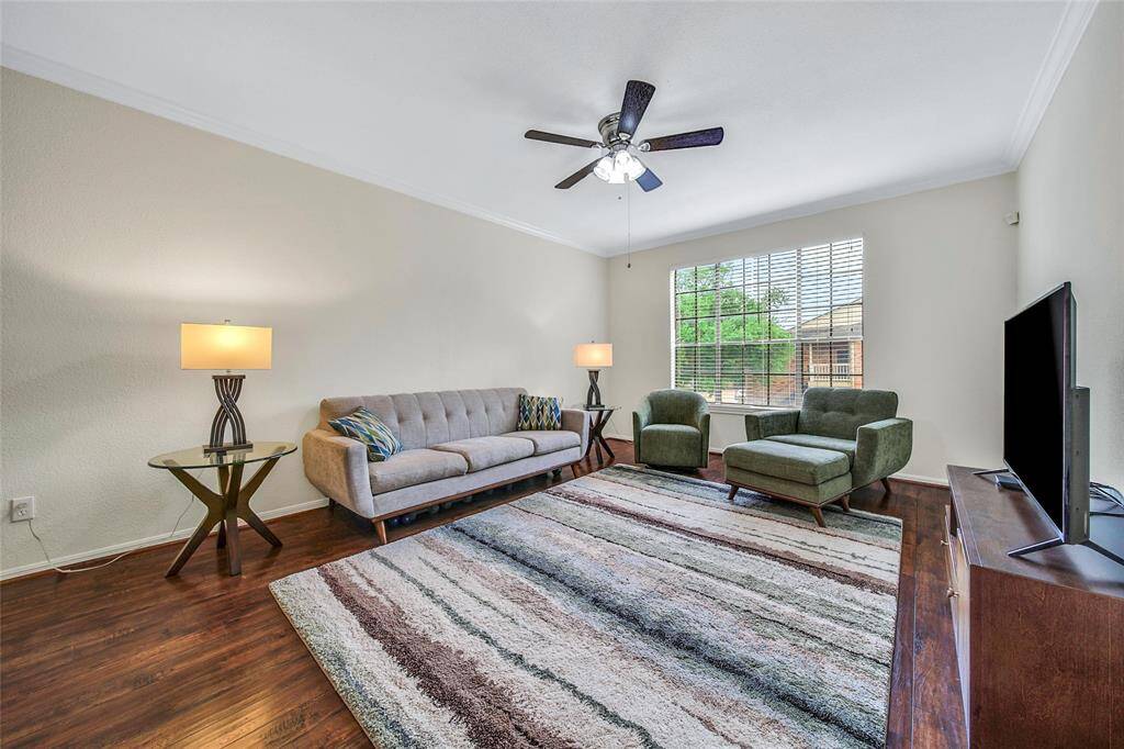 The light filled living room is a spacious and inviting gathering space, featuring rich wood look flooring and fresh neutral paint with crown molding.