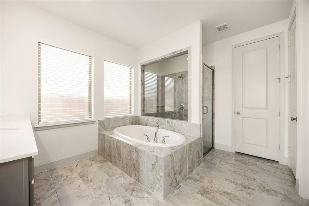 Indulge in relaxation within this spa-inspired primary bath, complete with a generous soaking tub, marble-style tile, and a sleek glass-enclosed shower.