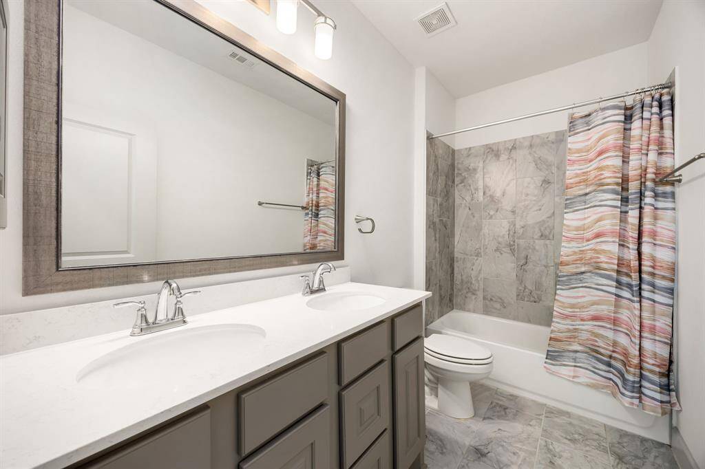 Bright and spacious full bathroom showcasing a dual-sink vanity, quartz countertops, and a tiled tub/shower combo.