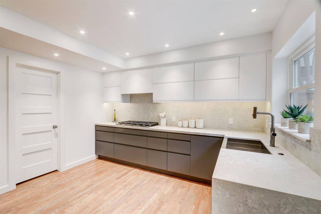 European two-toned style cabinetry, waterfall ledge, stone backsplash and farmhouse sink give this kitchen a clean modern look.