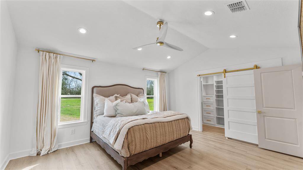 The spacious primary suite features gorgeous floors, high ceilings, recessed lighting, an upgraded fan, and two picture windows that overlook the expansive yard.