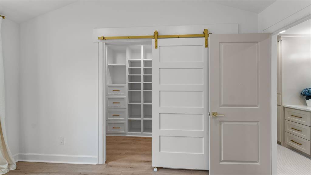 With a gentle push, the sliding door with sophisticated gold hardware glides open effortlessly, revealing the spacious and well-organized interior of your custom walk-in closet.