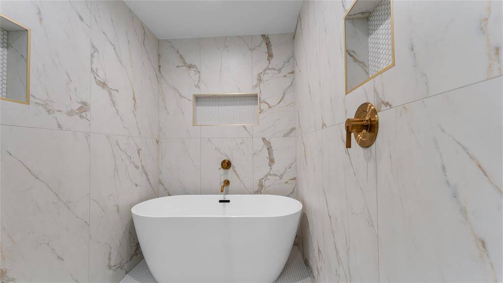 The sleek and modern freestanding bathtub is seamlessly integrated into the design of the spa-like shower area. Take note of the gorgeous marbled tile surround with gold finishes and beautiful tile accents located inside the strategically placed cut out niches that offer a spot to store shampoo, conditioner, and other essentials.