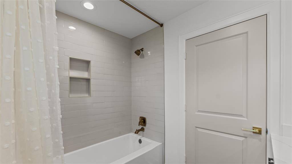 The tub/shower combination is fully customized with a gorgeous glossy tile that extends all the way up to the ceiling. Other features include strategically placed niches for your bathing essentials, and gold hardware!