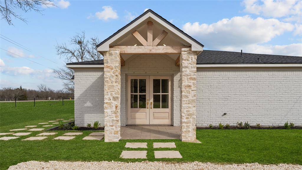 The private driveway leads to the side of the house that features another charming porch with stone wrapped pillars, exposed wood beams, and a pair of inviting double doors that lead you inside.