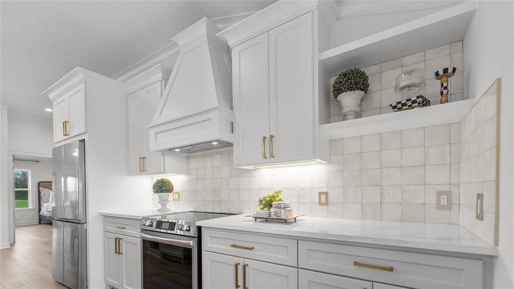 You have an electric range with ancustom vent hood that matchesthe white shaker-style cabinetry. Your eyes are immediately drawn to the white glossy tile backsplash that spans the length of the kitchen. The finish adds a touch of sophistication and modernity to the space, while also providing a practical surface that's easy to clean and maintain. Don't miss the under-cabinet lighting!