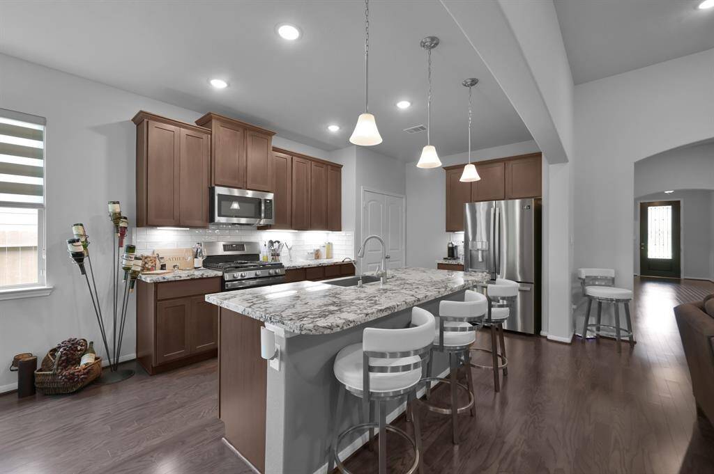 This kitchen features modern stainless steel appliances, an elegant granite countertop island with a place for seating, and warm wooden cabinetry. The open layout and pendant lighting create a welcoming atmosphere, perfect for entertaining.