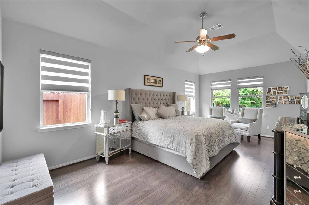 This spacious primary bedroom features a neutral color palette, hardwood floors, and ample natural light.