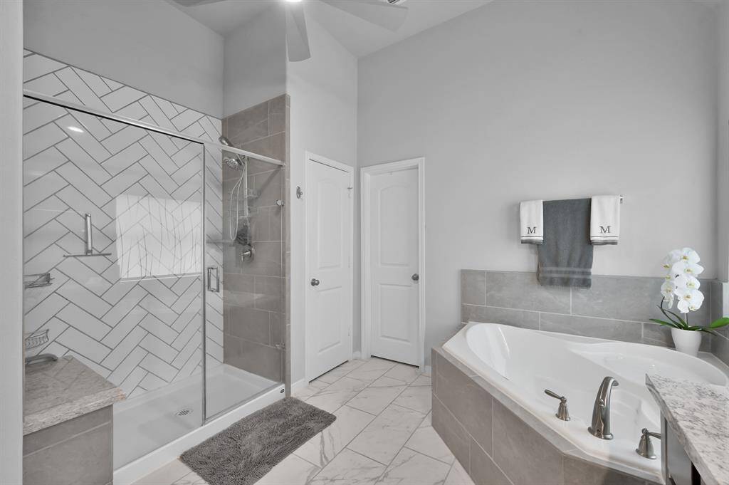 This modern bathroom features a spacious glass-enclosed shower with herringbone tile, a luxurious soaking tub, and sleek fixtures, all set against a stylish neutral palette.