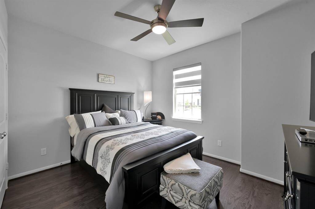 This secondary bedroom is cozy, has a ceiling fan, and a window with natural light. The room has a clean, neutral color palette and hardwood floors.