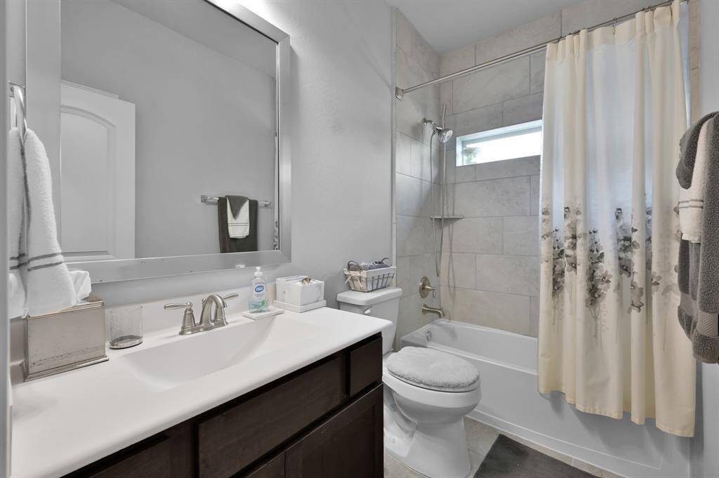 This secondary bathroom features a sleek vanity with ample counter space, a large mirror, and contemporary fixtures. The shower-tub combo is complemented by stylish tilework.