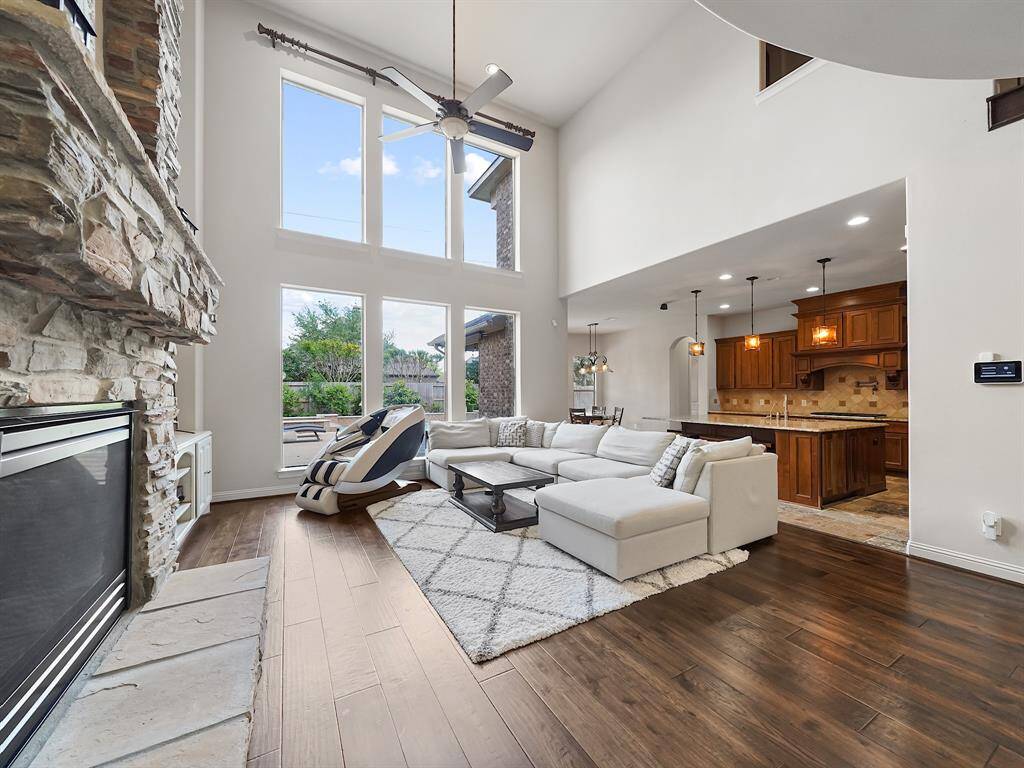 The immaculate two-story living room serves as the heart of the home, showcasing a floor-to-ceiling stone fireplace as its focal point. A dramatic two-story wall of windows floods the space with natural light and provides breathtaking views of the backyard oasis.