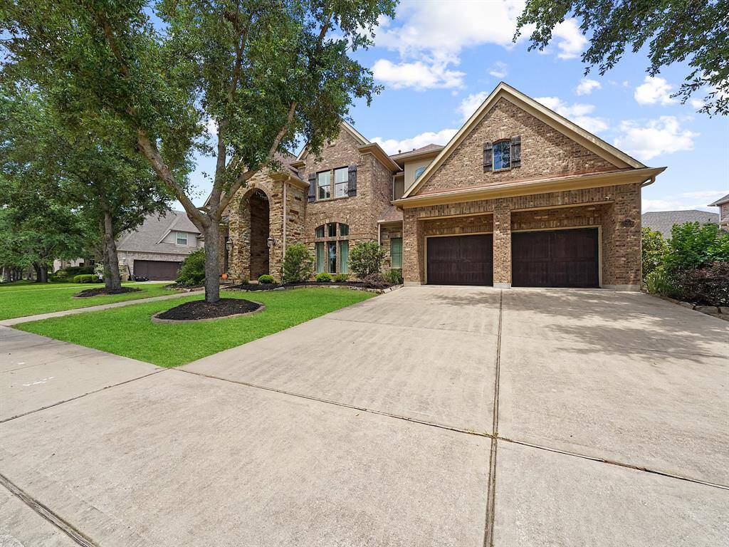 The property showcases stunning curb appeal with a stone and brick exterior, mature trees, and lush landscaping. A spacious three-car garage with tandem parking provides ample space for vehicles.