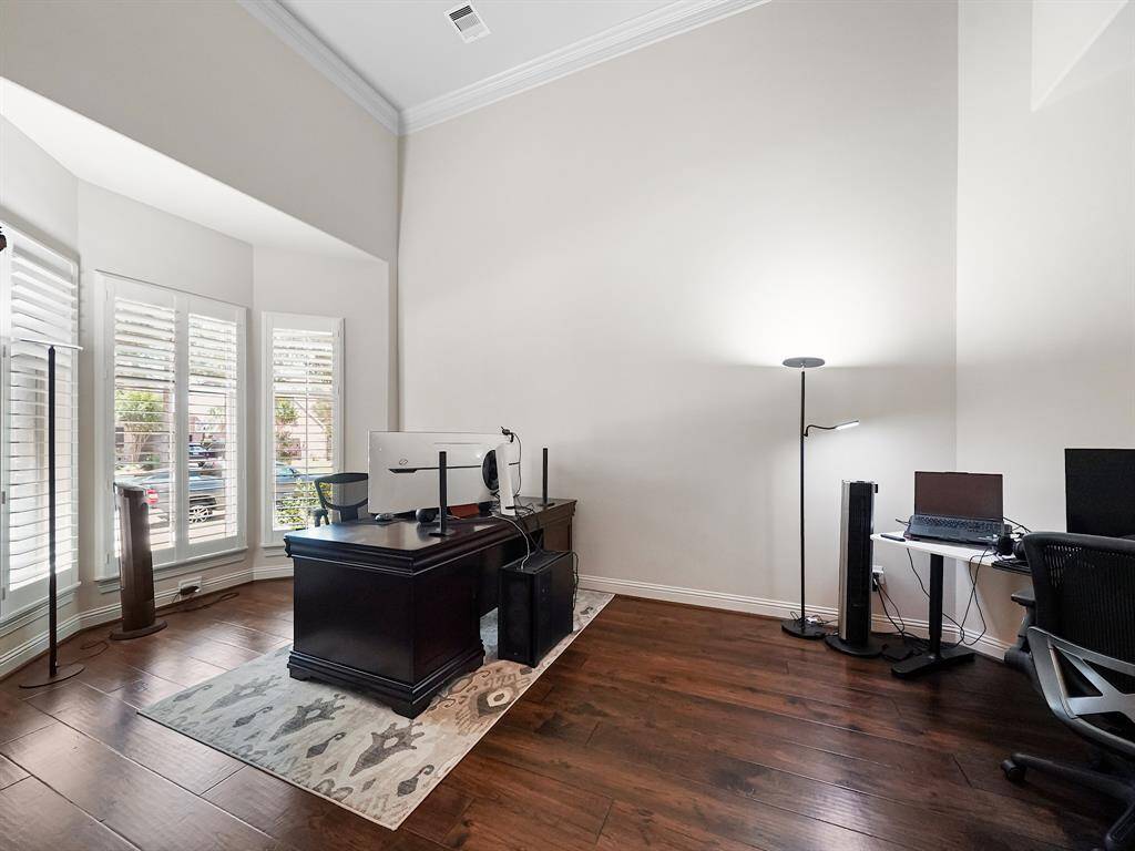 A private study, conveniently located off the entry, offers a tranquil space for work or reflection, enhanced by a soaring ceiling, intricate crown molding, a charming bay window, and elegant plantation shutters.