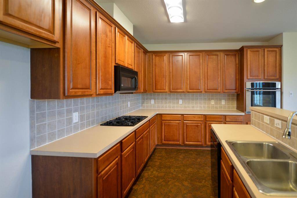 Spacious kitchen with ample wood cabinets, elegant tile backsplash, and comfortable cork flooring.