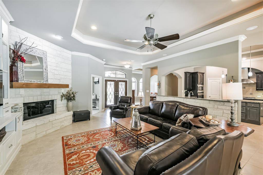The space features tray ceilings with recessed lighting and crown molding for a refined touch. A custom built-in entertainment center and a white stone fireplace with a wood mantel add both charm and functionality.