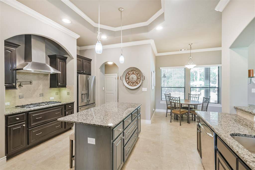This chef-style kitchen stuns with granite countertops, rich dark cabinetry, and a spacious center island with seating. Stainless steel appliances, a gas cooktop with pot filler, and double ovens add both function and flair. Tray ceilings, pendant lighting, and arched details elevate the space, while the open layout flows seamlessly into the breakfast nook and adjacent living areas. Perfect for everyday living and entertaining alike.