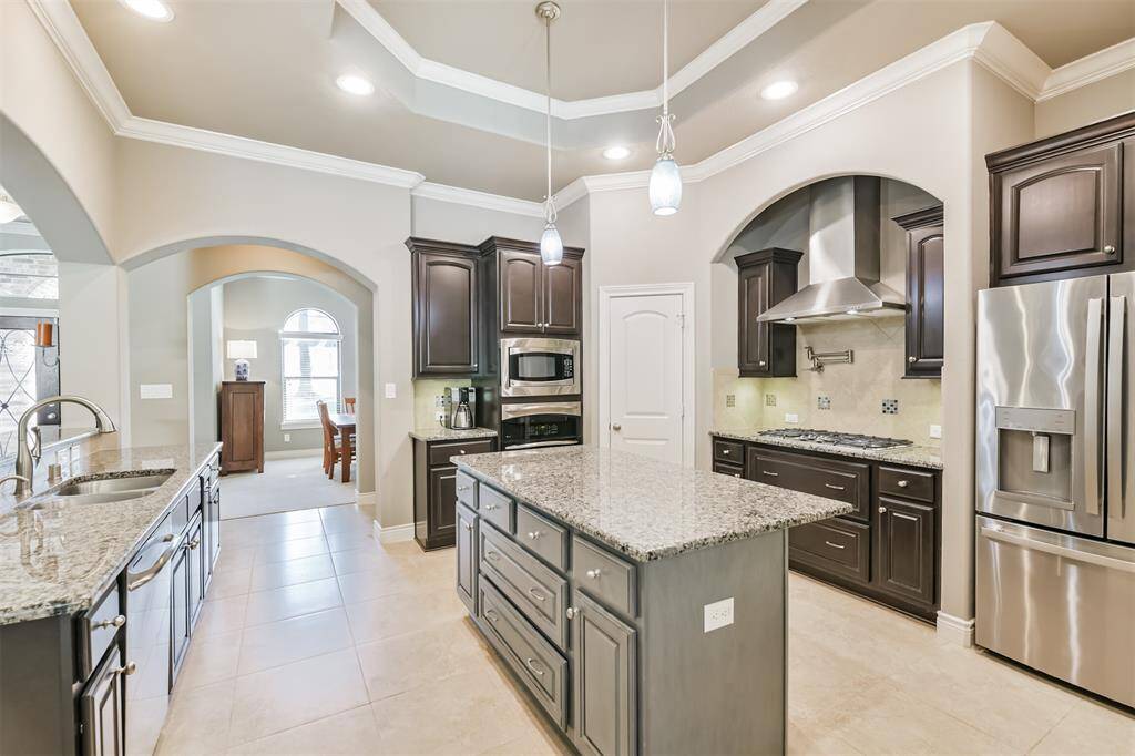 This gorgeous kitchen is the heart of the home, featuring rich cabinetry, sleek granite countertops, and a spacious center island with bar seating. Stainless steel appliances, a built-in double oven, and a 5-burner gas cooktop with pot filler elevate both style and functionality. Elegant pendant lighting, a walk-in pantry, and a custom vent hood complete the space.