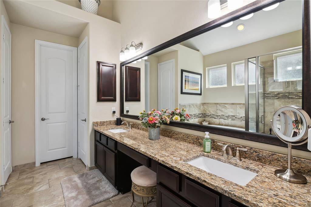The primary bathroom features dual sinks, a sitting area, a framed mirror, linen closet, and granite countertops.