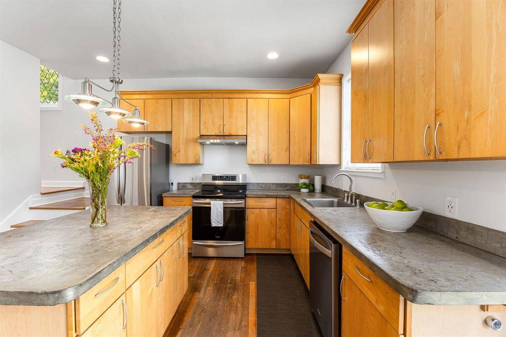 Recessed lighting, hardwood flooring, neutral wood cabinetry and cement counters with natural light flowing in. Island has enough space for counter height stools.