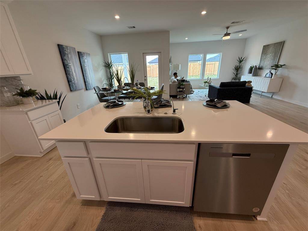 This modern bathroom features a sleek design with a white vanity, a large mirror, and a bathtub with elegant marble-patterned tiles. The space is bright with natural wood-style flooring and accented with greenery for a fresh touch.
