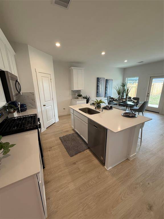 Bright and inviting living room with large windows, wood flooring, and tasteful furnishings. It features a ceiling fan, cozy seating area, and a stylish rug, creating a warm atmosphere.