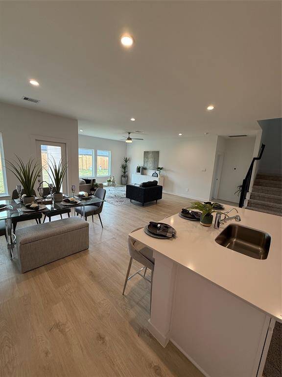 Bright and inviting living room with large windows, light wood floors, and neutral decor. Features a ceiling fan, comfortable seating, and access to the backyard. Perfect for relaxing and entertaining.