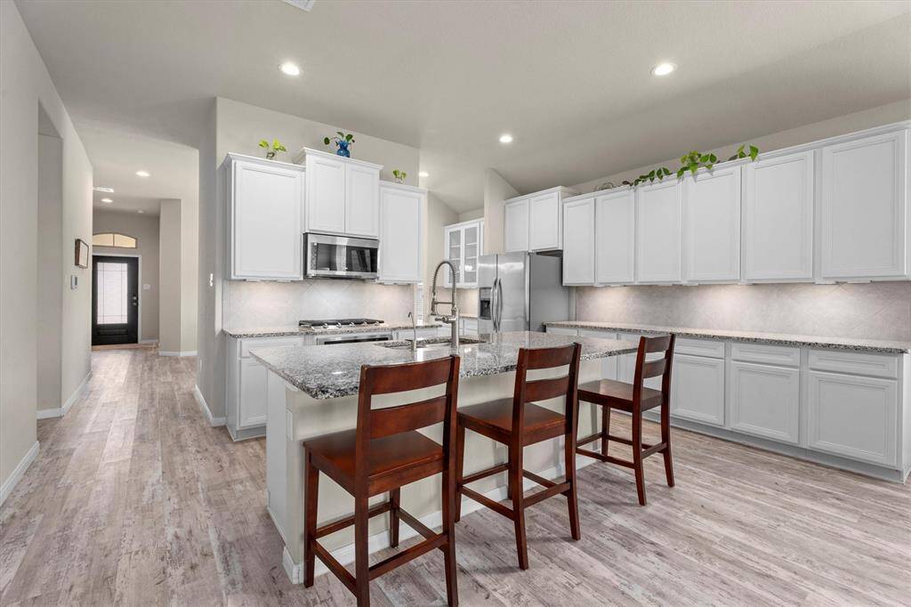 Discover a kitchen with a spacious island featuring a sink and breakfast bar. Enjoy cooking on a 5-burner gas cooktop and elegant granite countertops, illuminated by under-cabinet lighting.