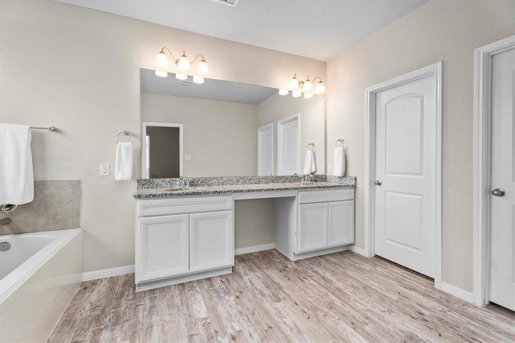 Experience luxury in this, spacious, primary en-suite bathroom featuring dual sinks separated by a vanity area and elegant granite countertops.