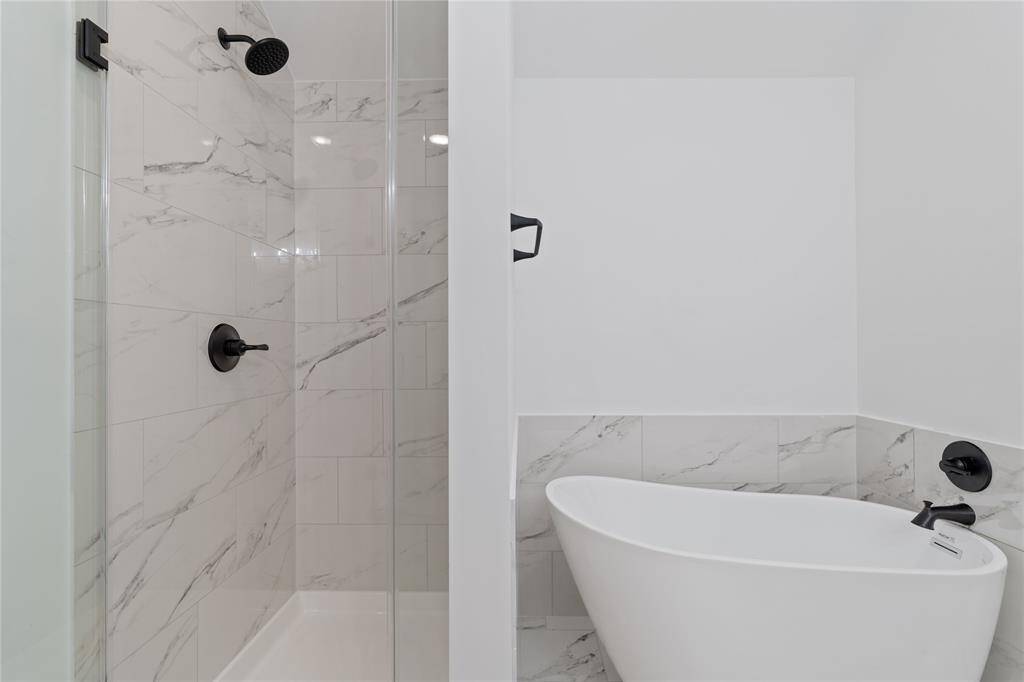 Adjacent to the tub, the large walk-in shower is framed by glass doors and features stunning tilework, providing both style and functionality.
