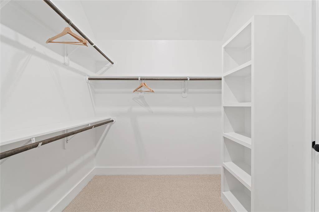 This spacious primary closet is designed for maximum organization, with ample hanging space on both sides and custom shelving for shoes, accessories, or folded clothing.
