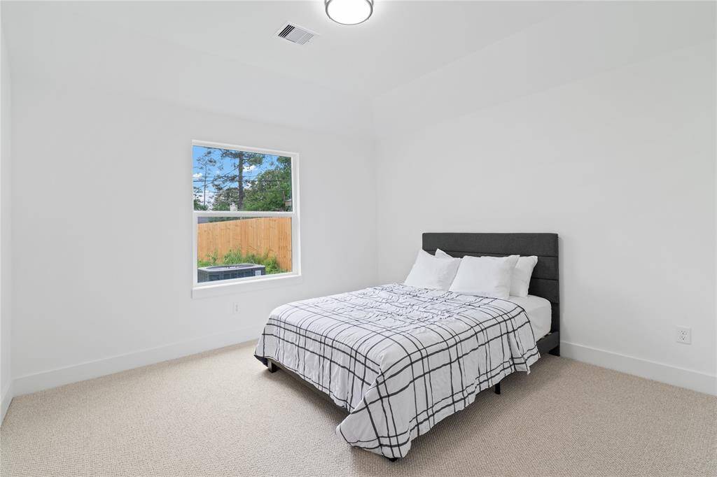This spacious second bedroom is filled with natural light, thanks to a large window that frames a serene view of the backyard.