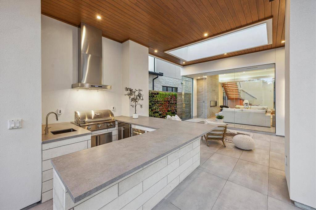 Summer kitchen equipped with grill, beverage fridge, sink, and trash and storage drawers