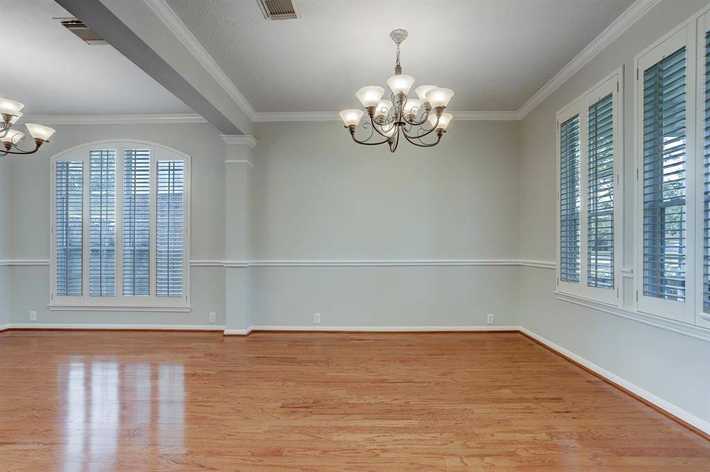 This spacious room features elegant hardwood flooring, large windows with plantation shutters, and stylish light fixtures, perfect for a dining or living area.