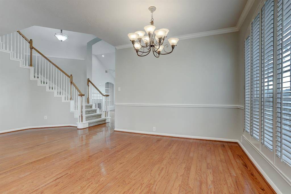 This inviting space features beautiful hardwood floors, a classic chandelier, and large windows with shutters that allow ample natural light. The elegant staircase with wooden railings adds charm and character to the room.