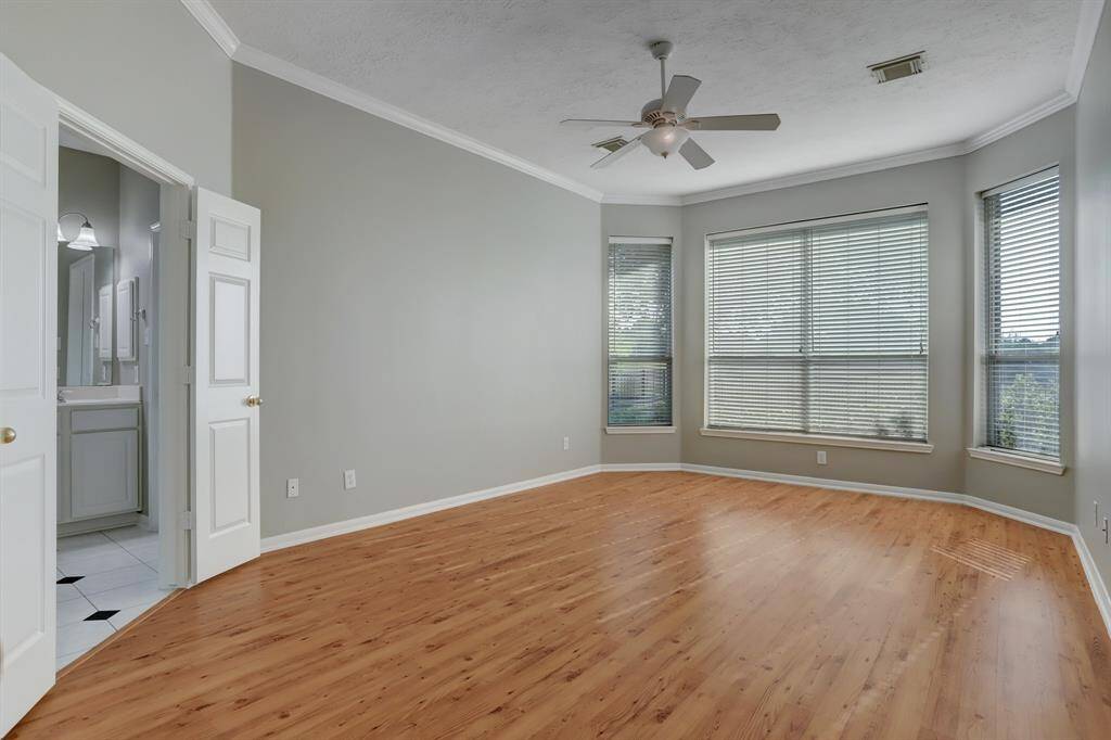 Bright, spacious bedroom with large windows, wood flooring, and a ceiling fan. Features a neutral color palette and an en-suite bathroom with double doors.